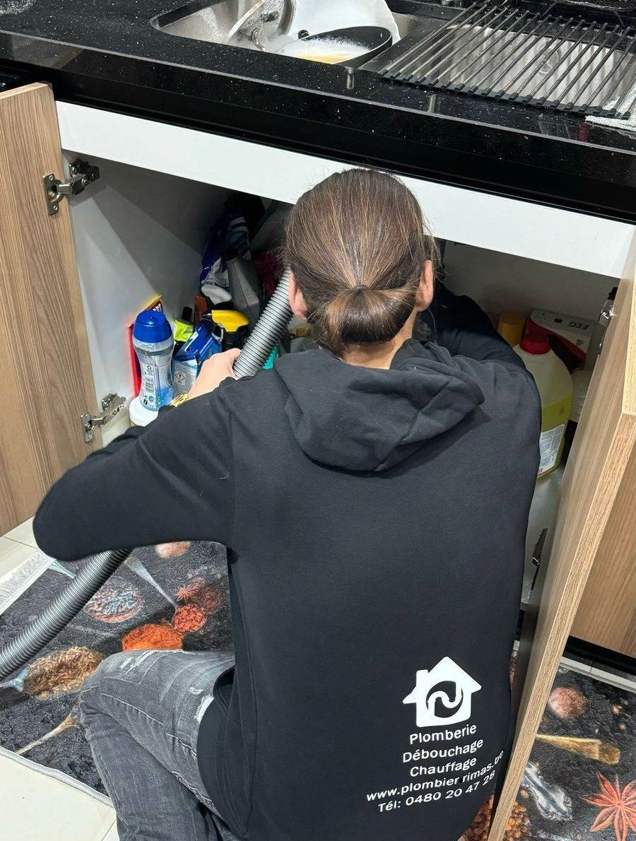 Plombier Liège réparant une fuite d'eau sous évier avec outils d'urgence service rapide et efficace à domicile