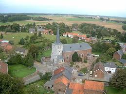 Camion de débouchage Faimes devant l'église St Pierre, rue typique bordée de maisons en briques rouges en fond.