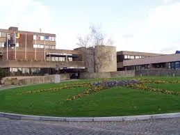 Plombier Sambreville réparant une canalisation devant l'Hôtel de Ville sous un ciel lumineux typique de la région belge.
